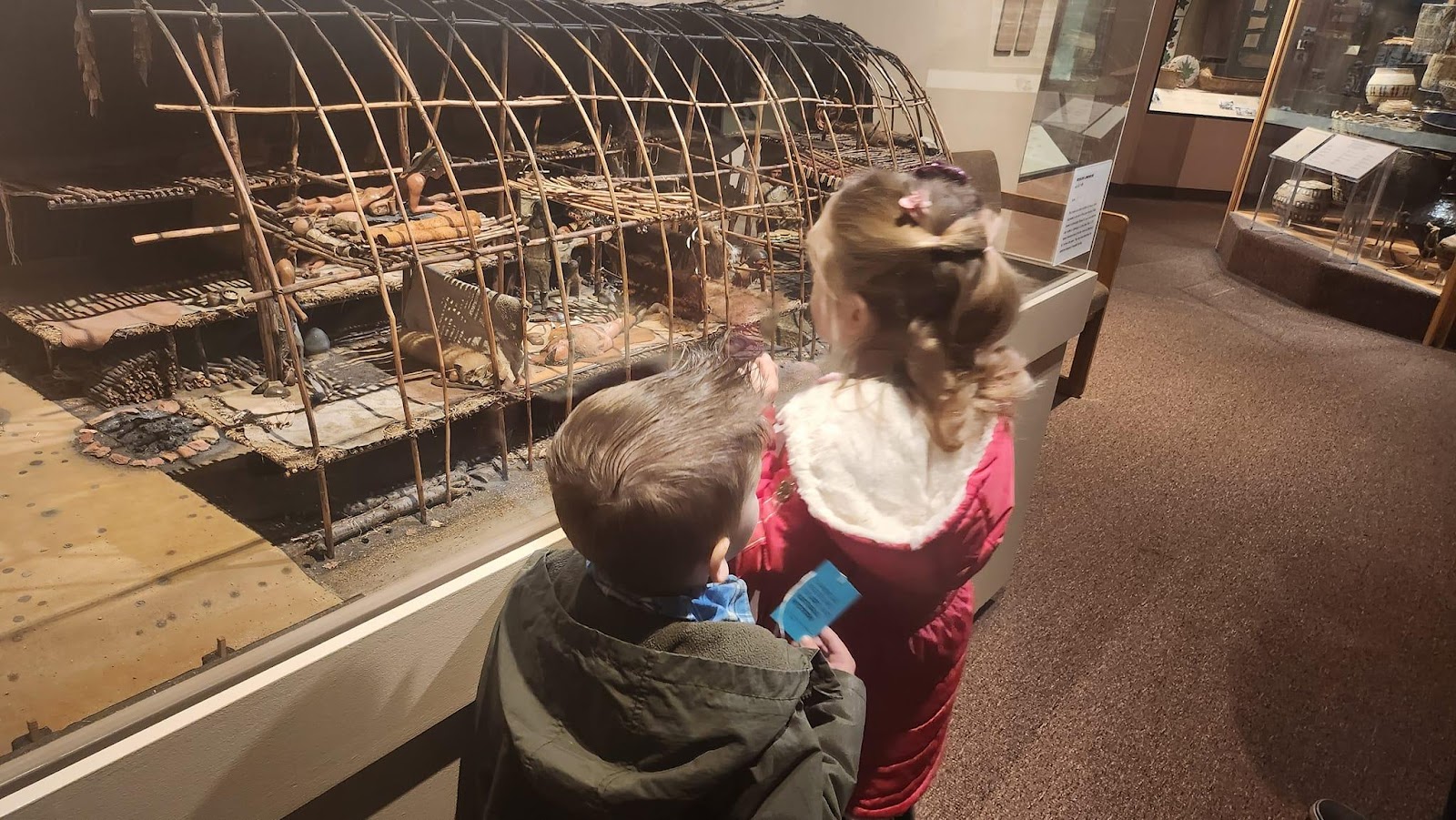 A child and child looking at a bird cageDescription automatically generated