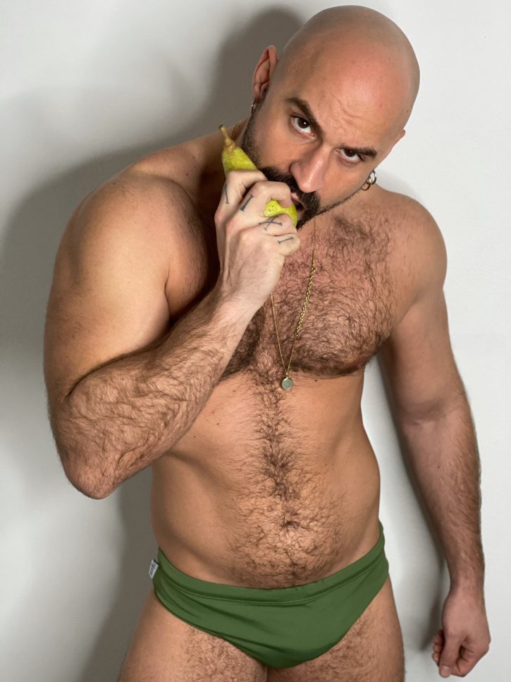 Mister Caccamo biting into a pear in green swim briefs showing off his gay hairy muscle daddy chest while leering at the camera