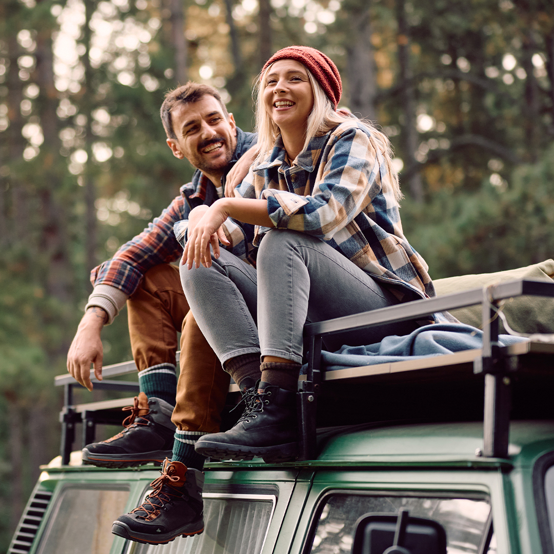 A happy couple sits atop a vehicle, admiring tall Redwood trees on a road trip from Redwood National Park to San Francisco.