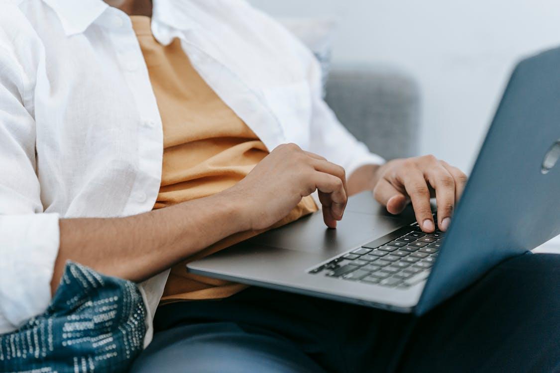 Free Crop unrecognizable male freelancer sitting on sofa while working on portable computer in light house Stock Photo