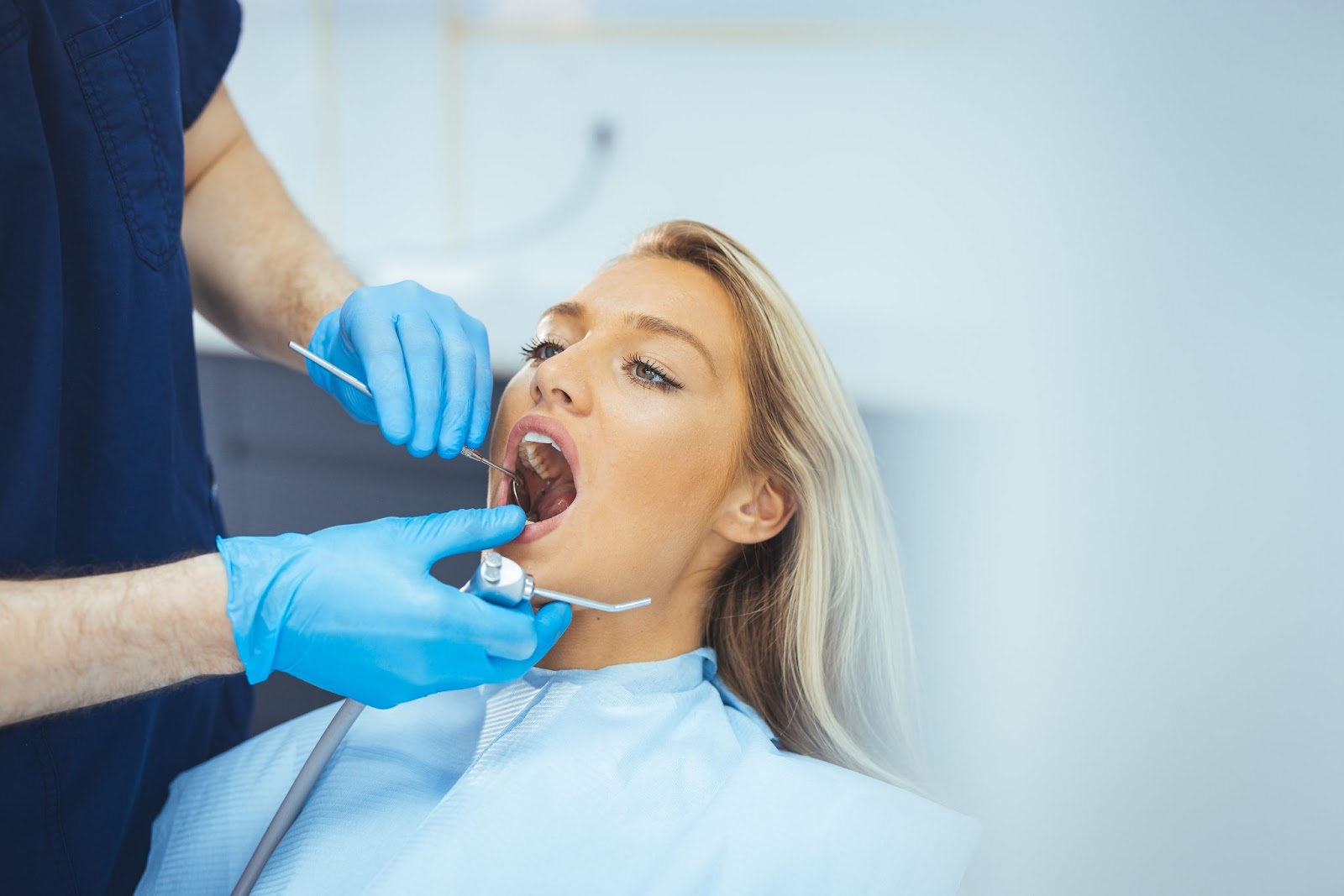 A young woman at the dentist getting examined for cavities.