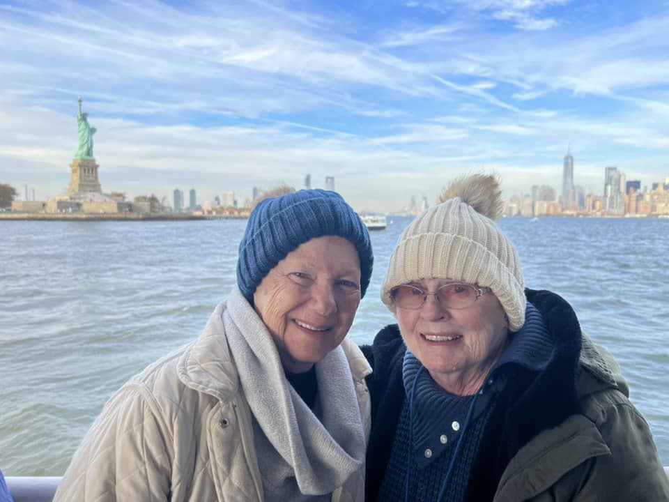 Two seniors walking together on a boat in front of the Statue of Liberty