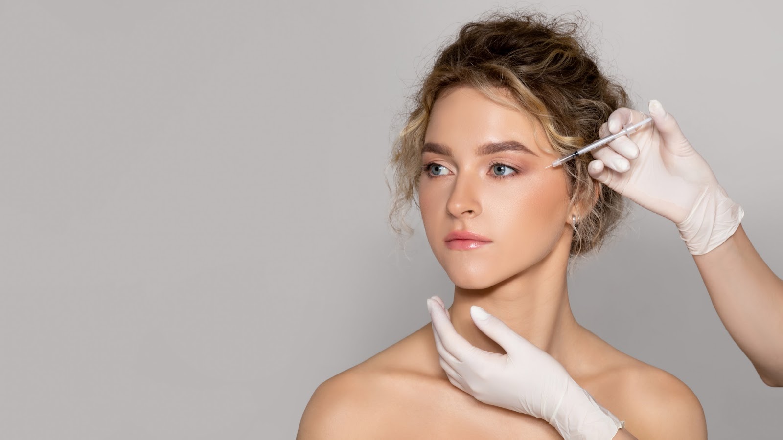 A young woman receives a Botox injection underneath her left eye.