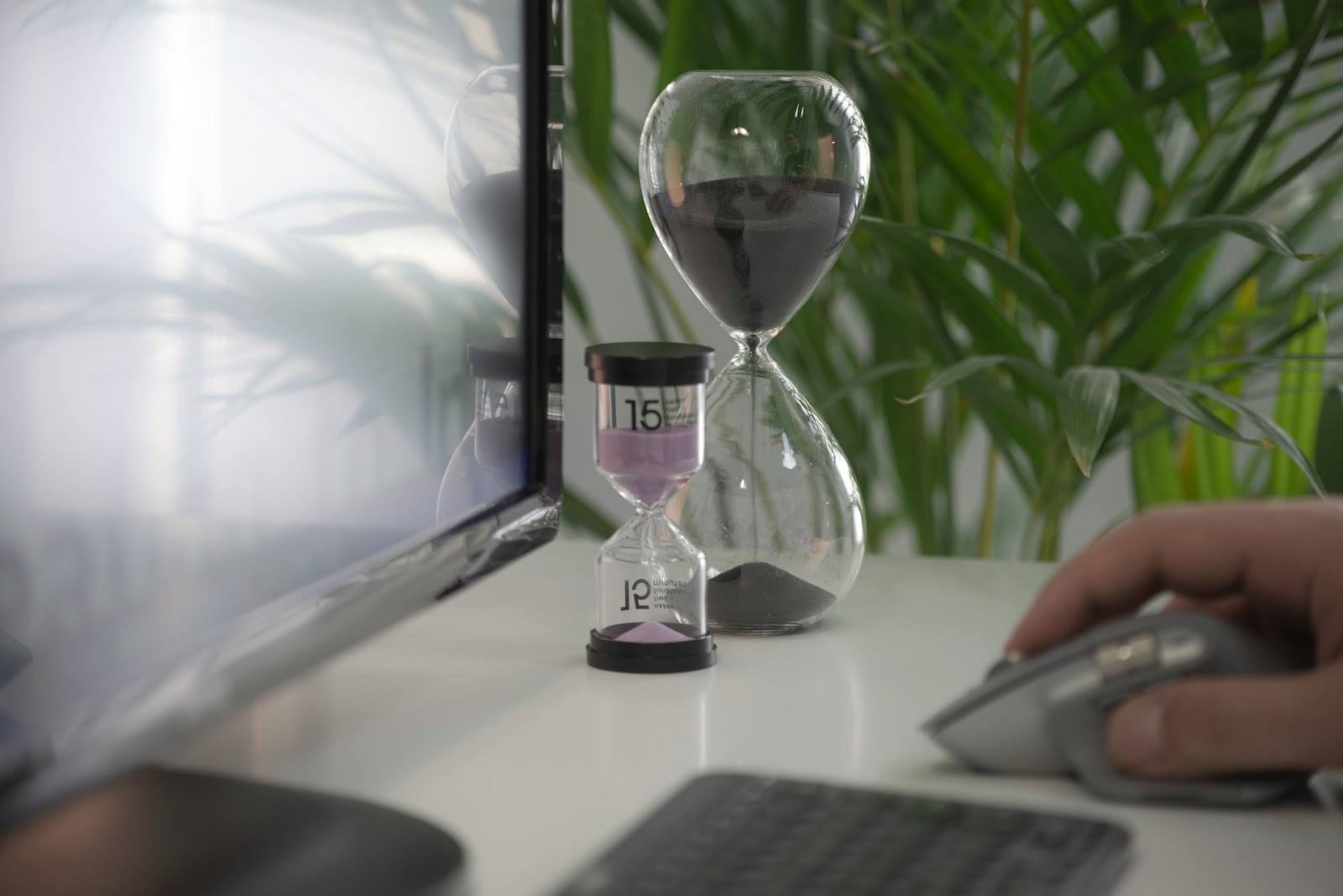 Minute and hour glasses near someone using a computer