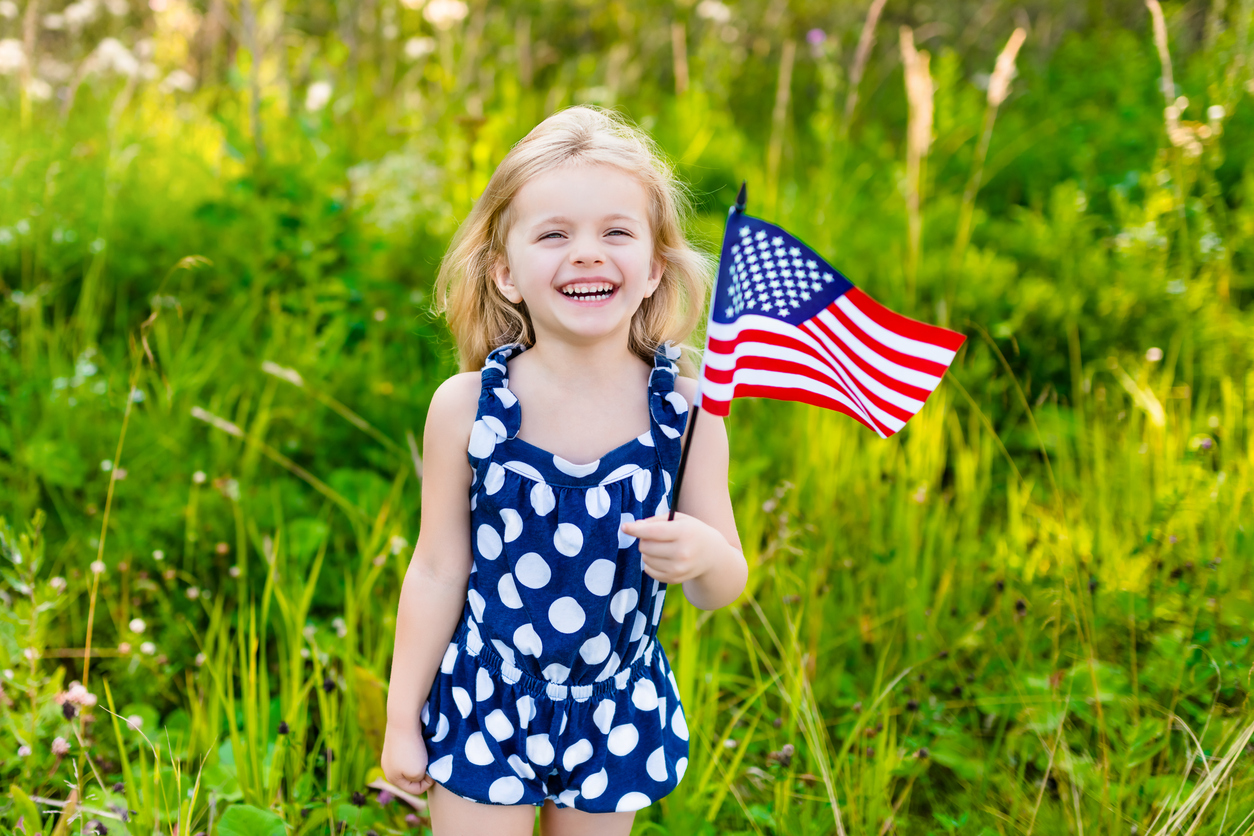 A young girl standing in a grassy field holding an American flag.