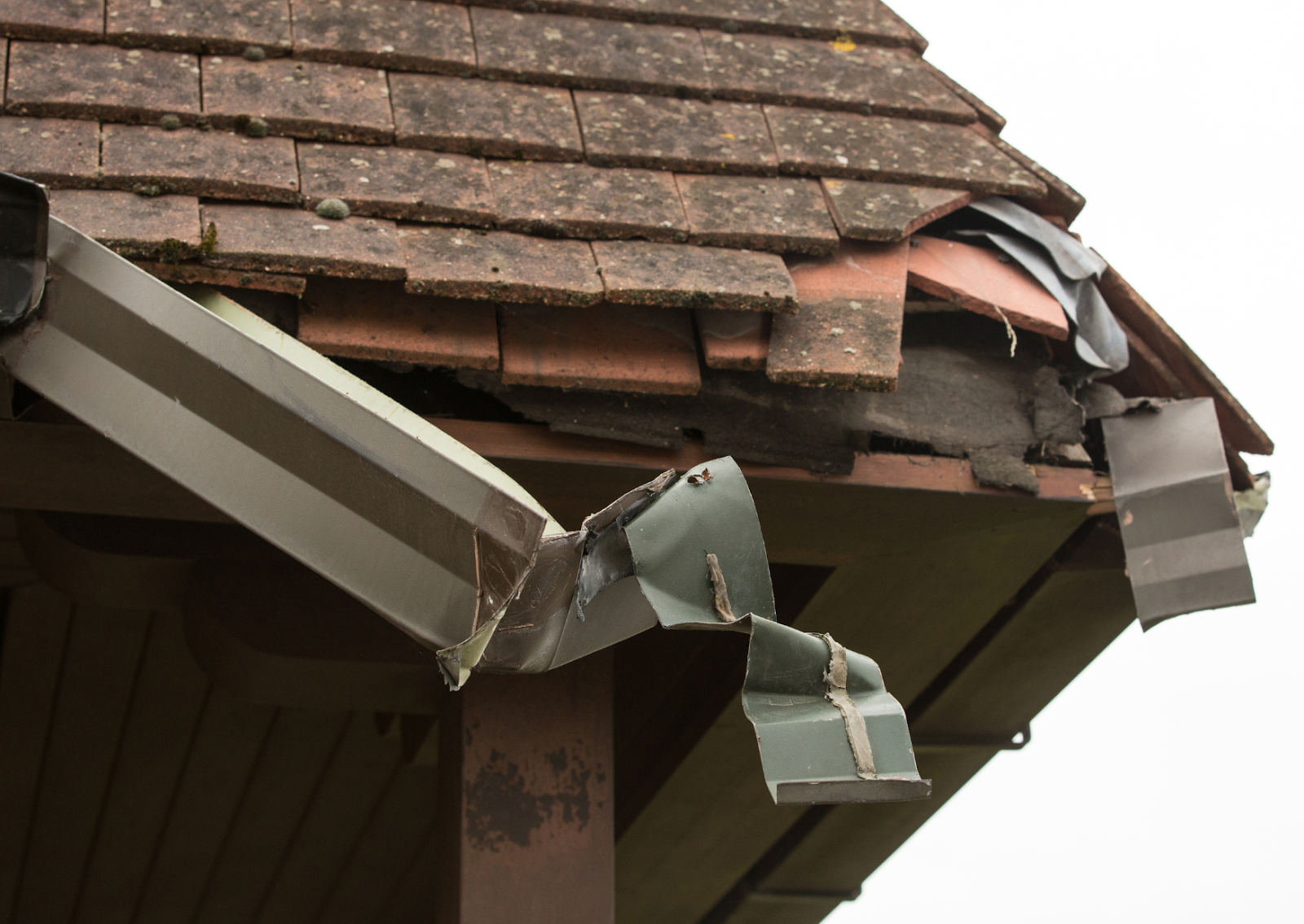 Damaged roof corner with broken shingles and gutter, indicating severe wear. How do I know if I need a new roof?