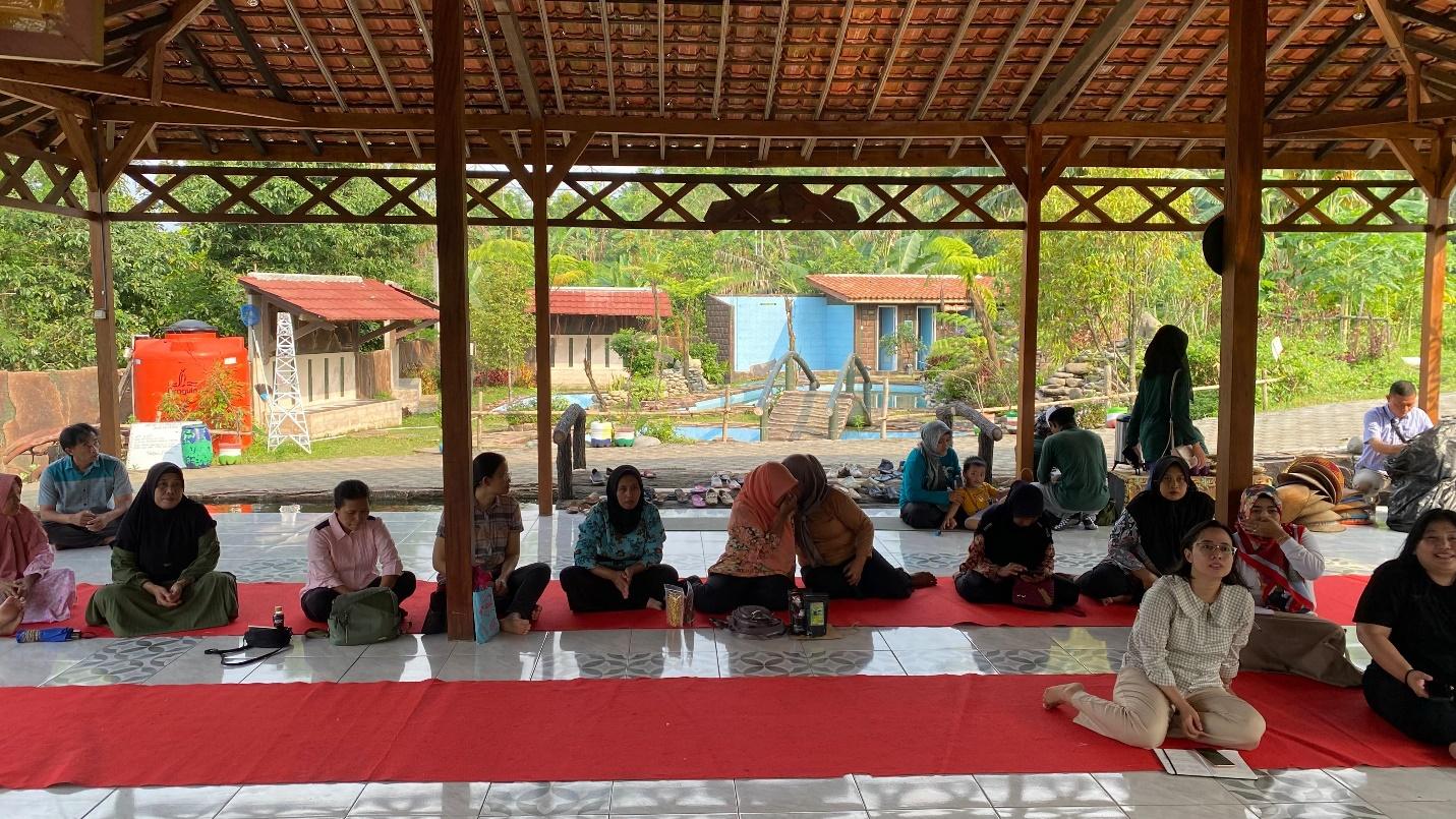 A group of people sitting on a red and white rug under a roof

Description automatically generated