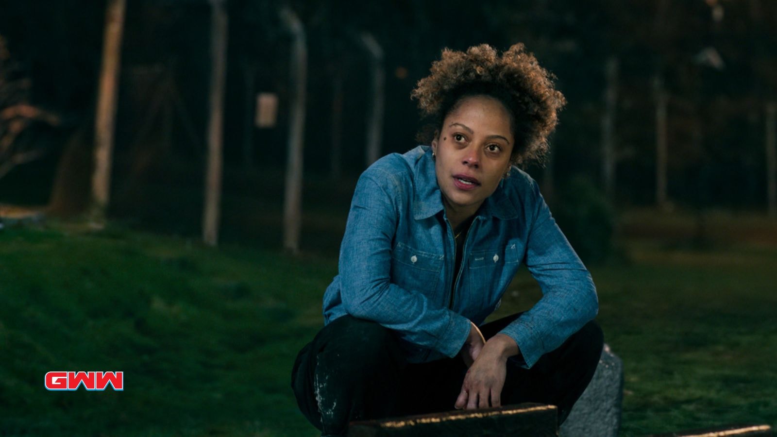 Louisa crouching outdoors at night, appearing thoughtful and concerned.