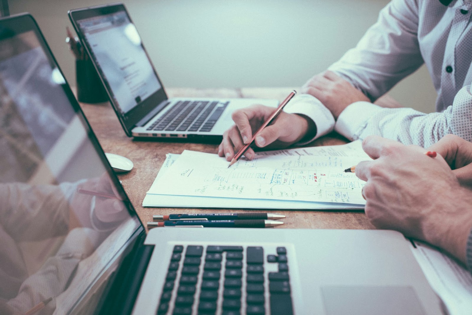 Dos personas trabajando en un escritorio con computadoras portátiles y documentos, analizando datos y tomando notas