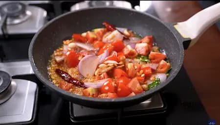 Cooking diced tomatoes and onions with spices to create a flavorful chutney base.