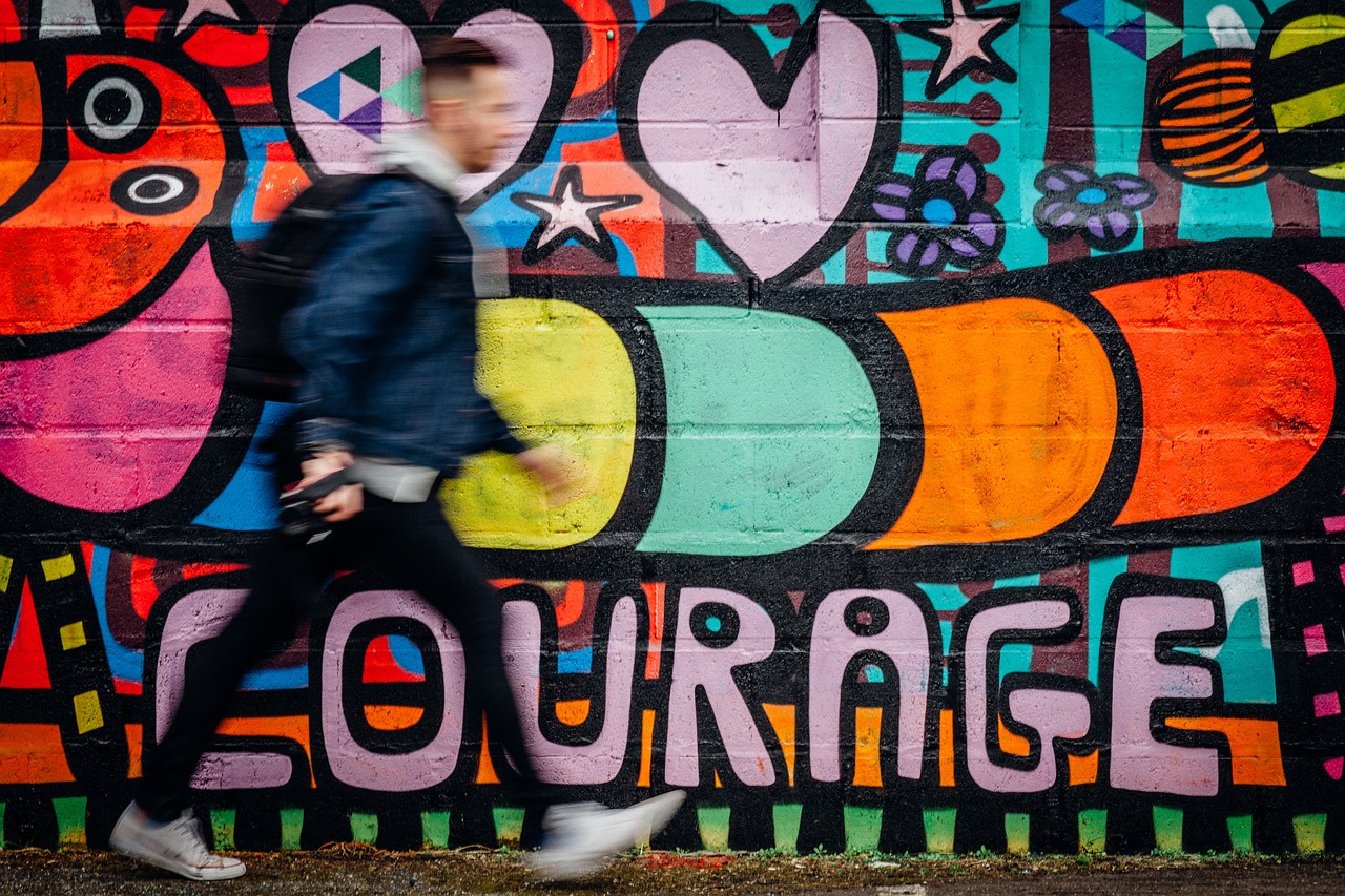 Photo of man walking past a colorful wall mural with the word courage.