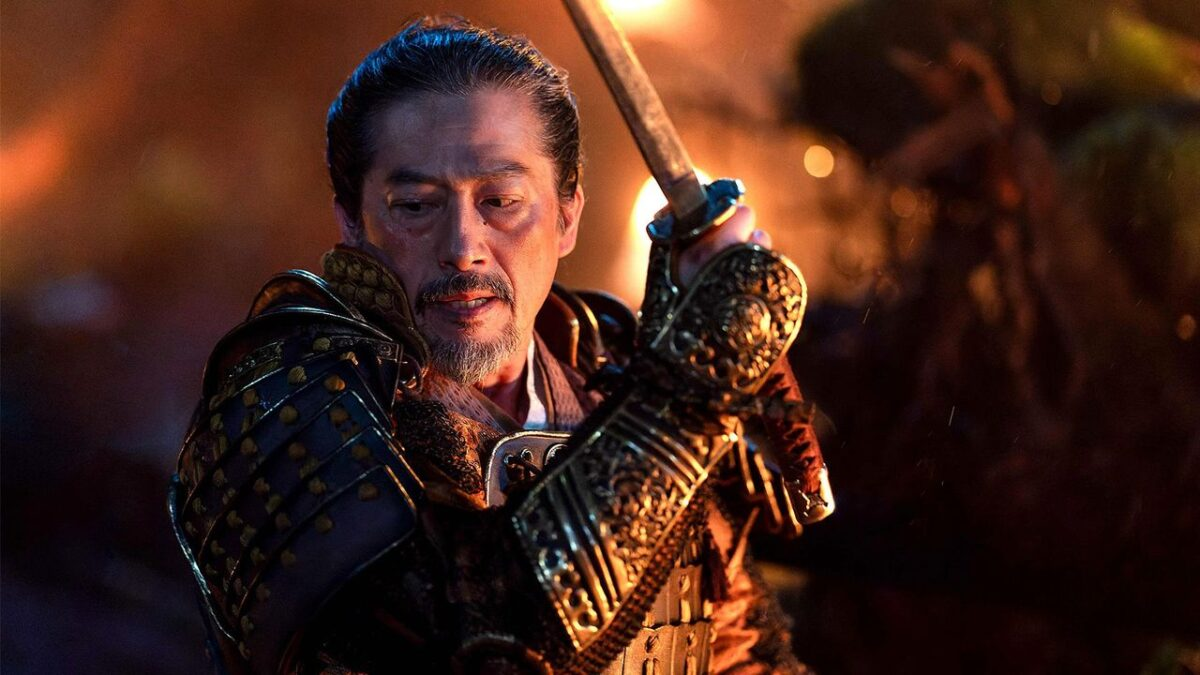 Guerrero samurái con armadura tradicional y empuñando una espada en una escena de batalla iluminada por fuego en el fondo.