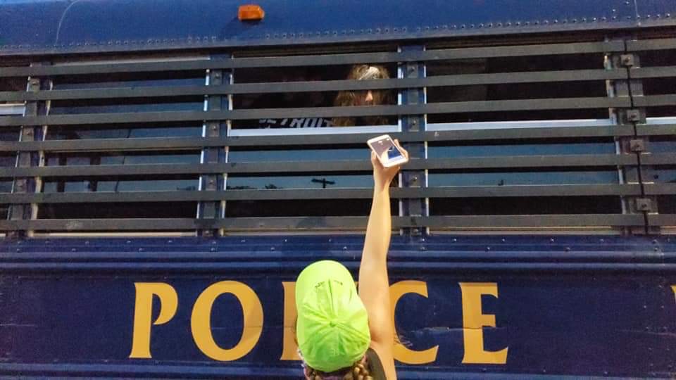 A lawyer holds up a phone to someone in a police van