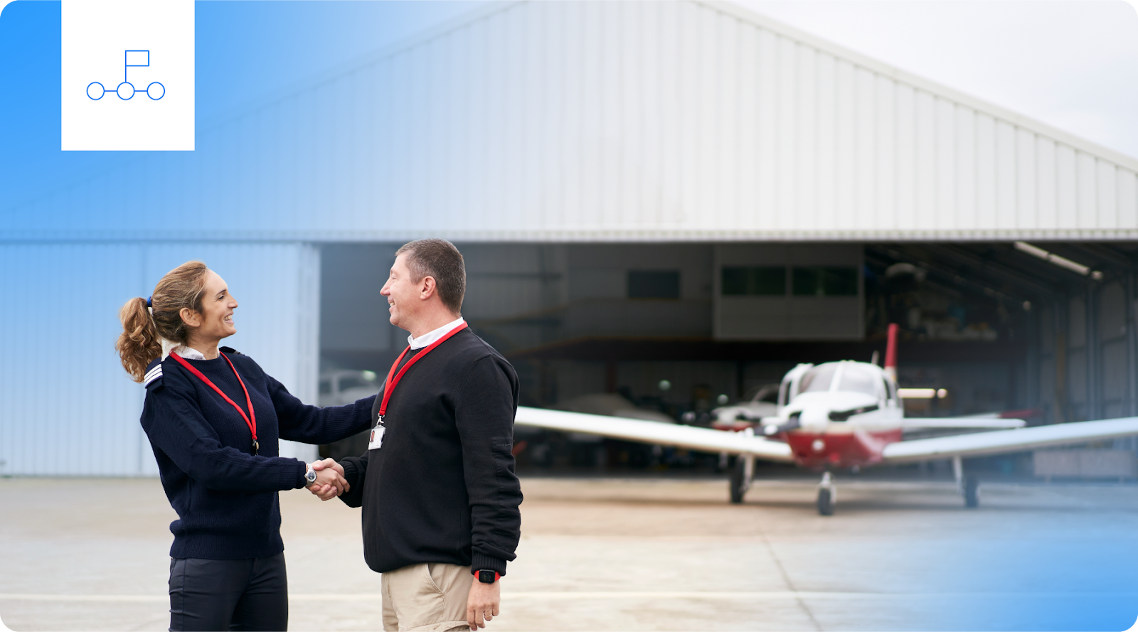 A flight instructor congratulates a student in front of an airplane hangar.