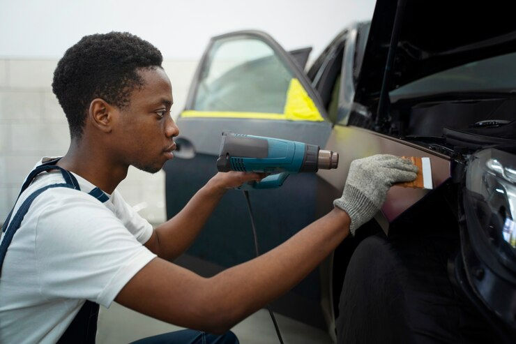 A man is using a heat gun to apply car wrap to a car.