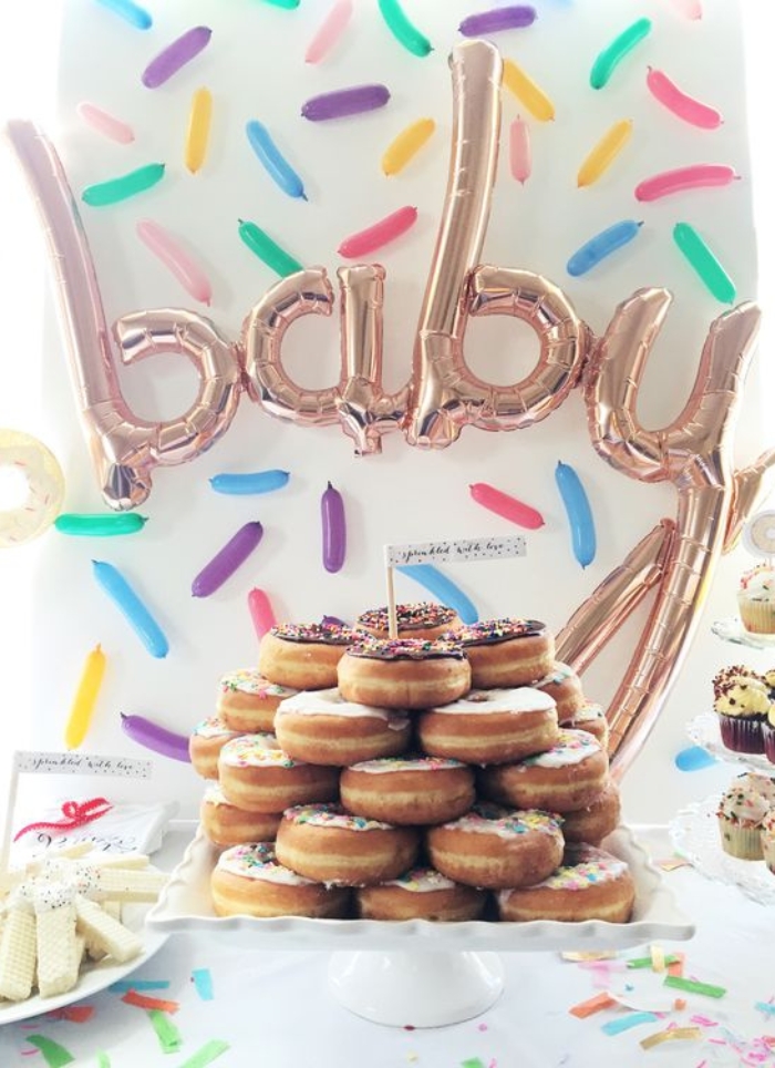 balloons shaped like baby hanging behind donuts on a white cake stand