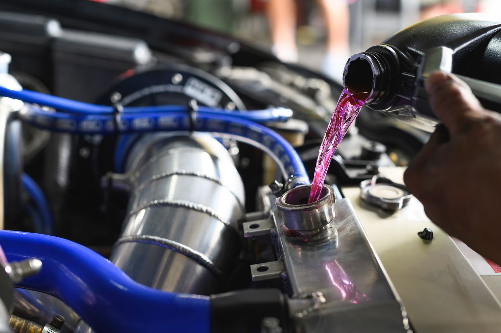 A close-up image of a mechanic topping off a radiator tank with purple coolant.