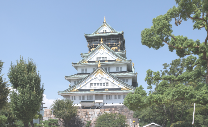 A large building with a stone wall and trees with Osaka Castle in the background

Description automatically generated