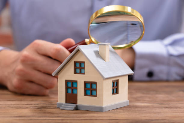 person holding magnifying glass with miniature house -real estate business