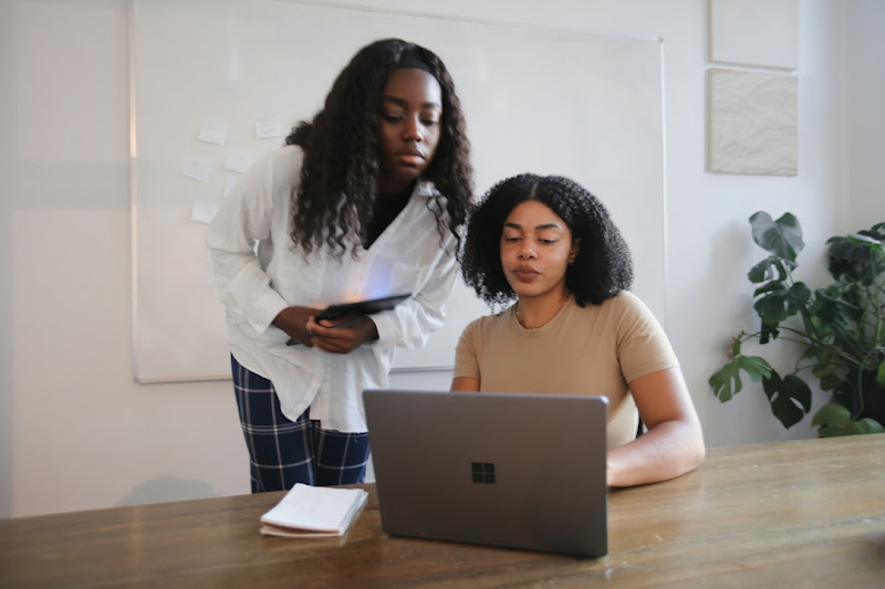 Two female colleagues huddled around a laptop, engaged in a discussion while comparing the distinctive features of Microsoft Search and Google.