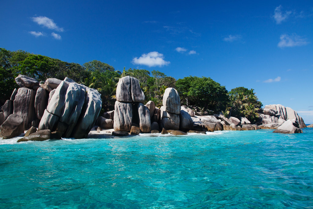 Beach with clear water and large rocks scattered along the shore.