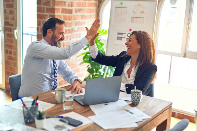 Two people sitting at a desk high-fiving