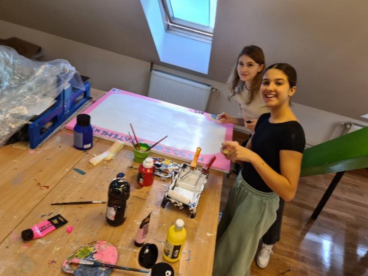 Two girls standing next to a table with paint and brushes

Description automatically generated