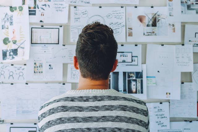 A man standing in front of a paper-covered wall, examining it closely probably to formulate a strategy.