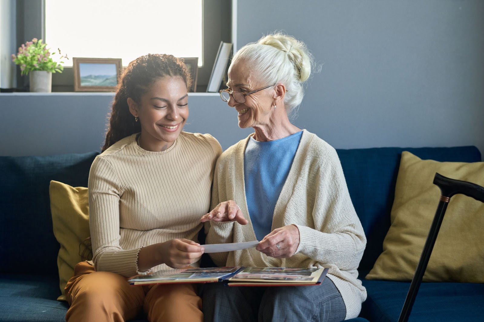  female senior reminiscing over old photos with her adult daughter at a senior living community.