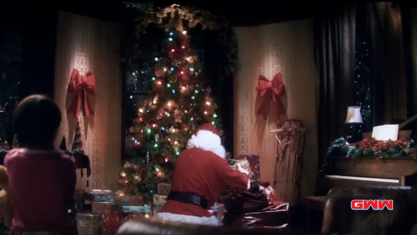 Child watching Santa from behind, room decorated for Christmas.