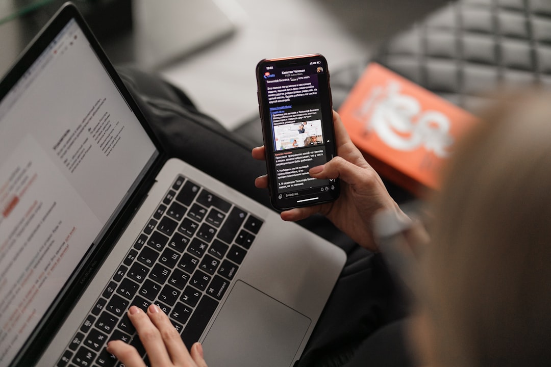 A person holding black phone in front of a laptop.