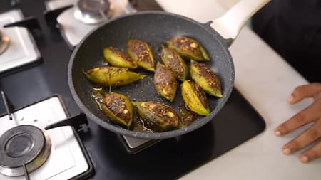 Cooking the stuffed bitter gourds in a pan.