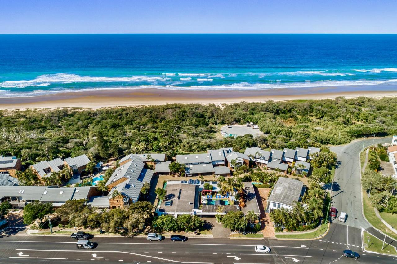 aerial view of Hideaway Noosa gay mens beach resort in Queensland australia with the resort's pool shown in the middle among other units and houses with the large seashore beach shown in the background via booking.com