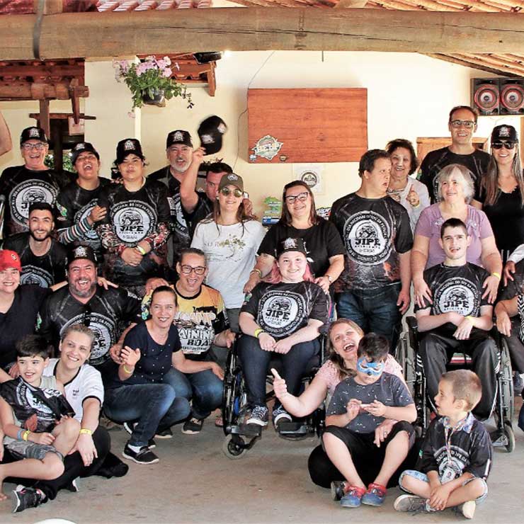 Grupo diverso de pessoas, incluindo crianças e adultos, reunidos e sorrindo em um evento, usando camisetas temáticas.