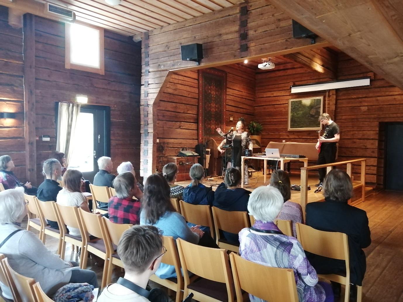 A group of people sitting in chairs in a room with a person playing a guitar

Description automatically generated
