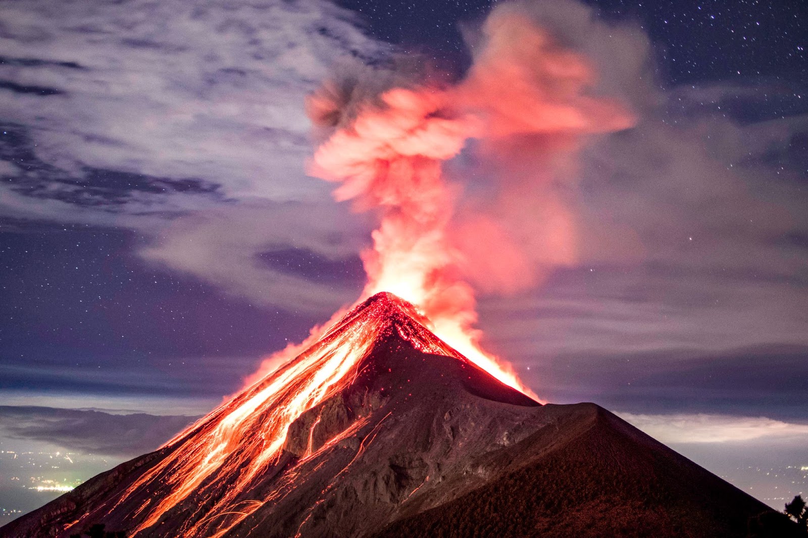 A volcano erupting at night, with lava flowing down its slopes and lighting up the sky with a fiery glow.