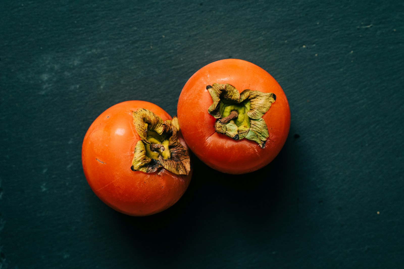 3 caquis rojos sobre tejido negro