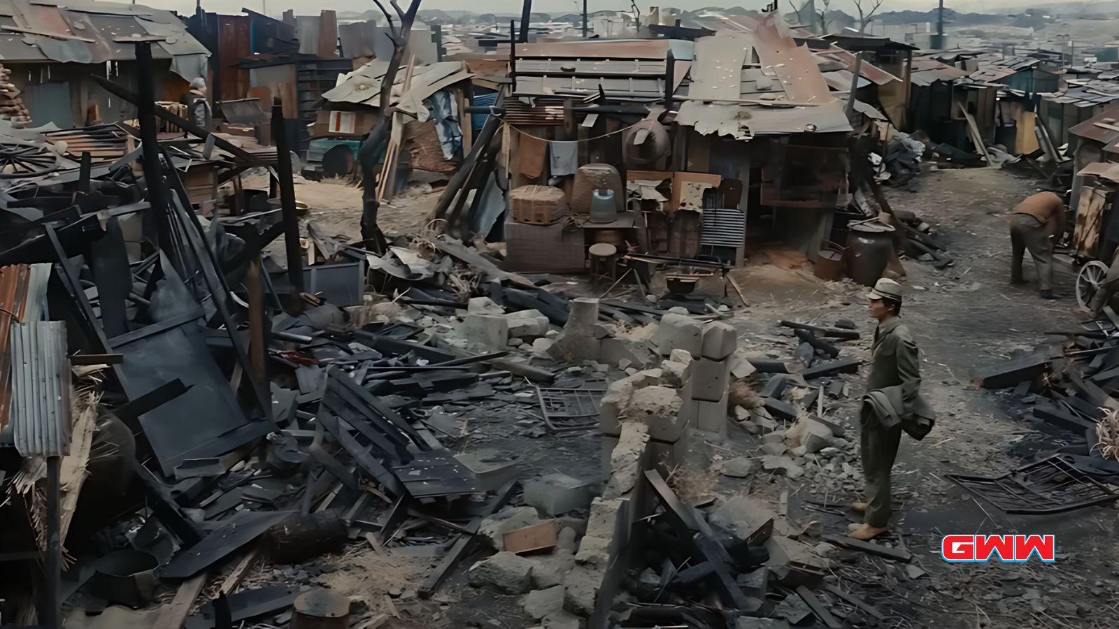 Koichi stands in a devastated village with ruins and debris.
