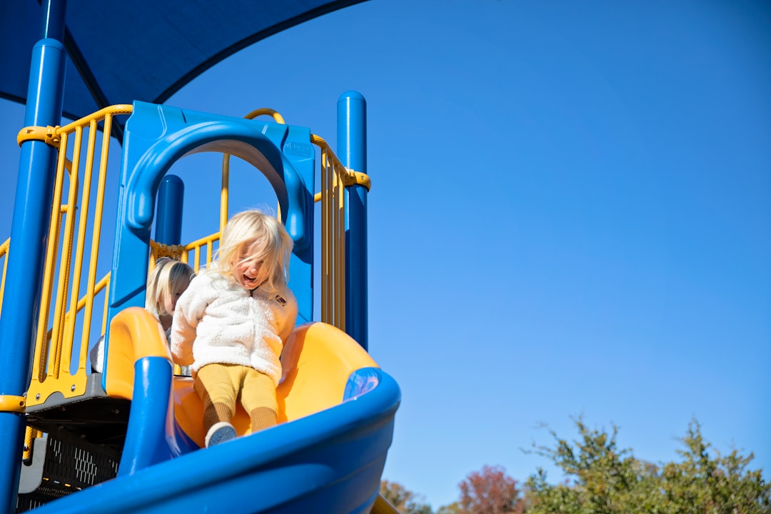 girl in yellow shirt riding blue plastic slide during daytime