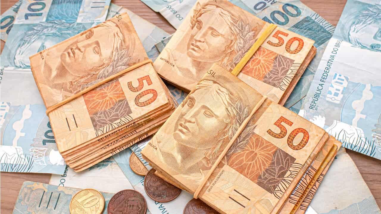 Cédulas de 50 envoltas em elástico amarelos, notas de 100 reais e moedas