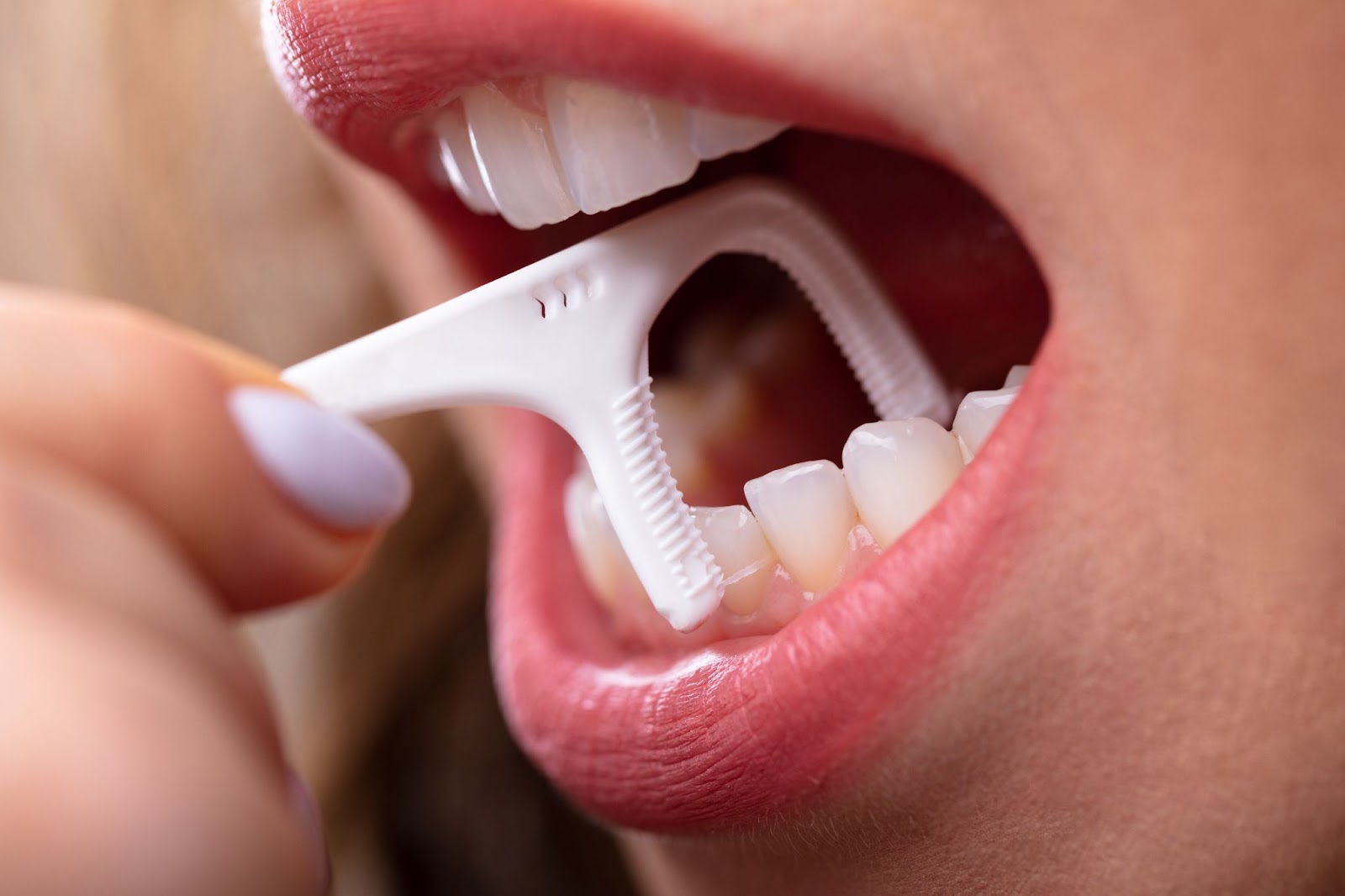 A close-up of a woman flossing her bottom teeth with a floss pick.