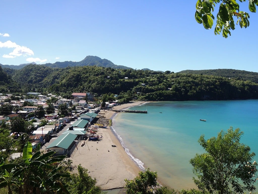 St. Lucia's, one of the safest Caribbean Islands showing sandy beach with houses in the corner and mountains beyond.