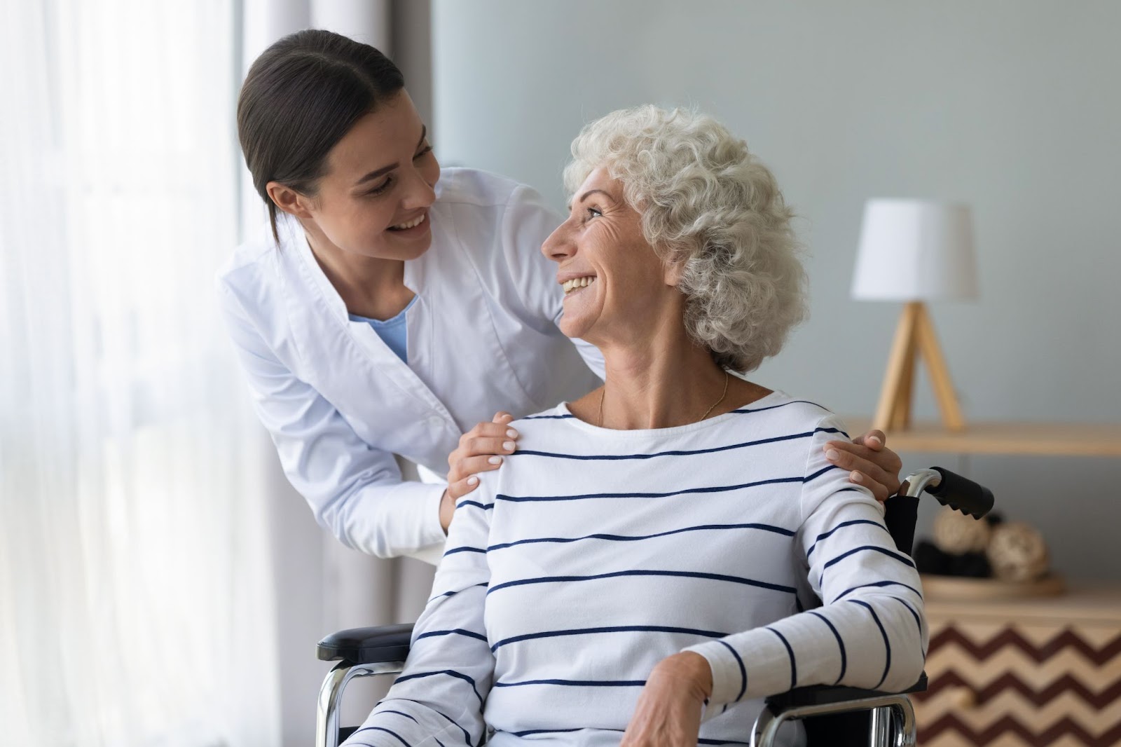 A caregiver in a senior living community checks in with a resident in a wheelchair.