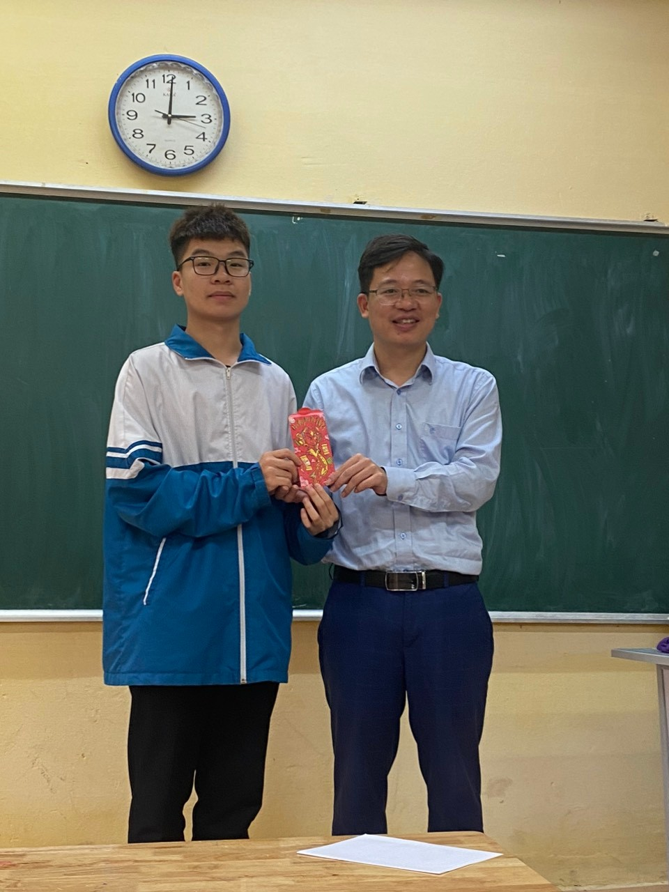 Two men standing in front of a chalkboardDescription automatically generated