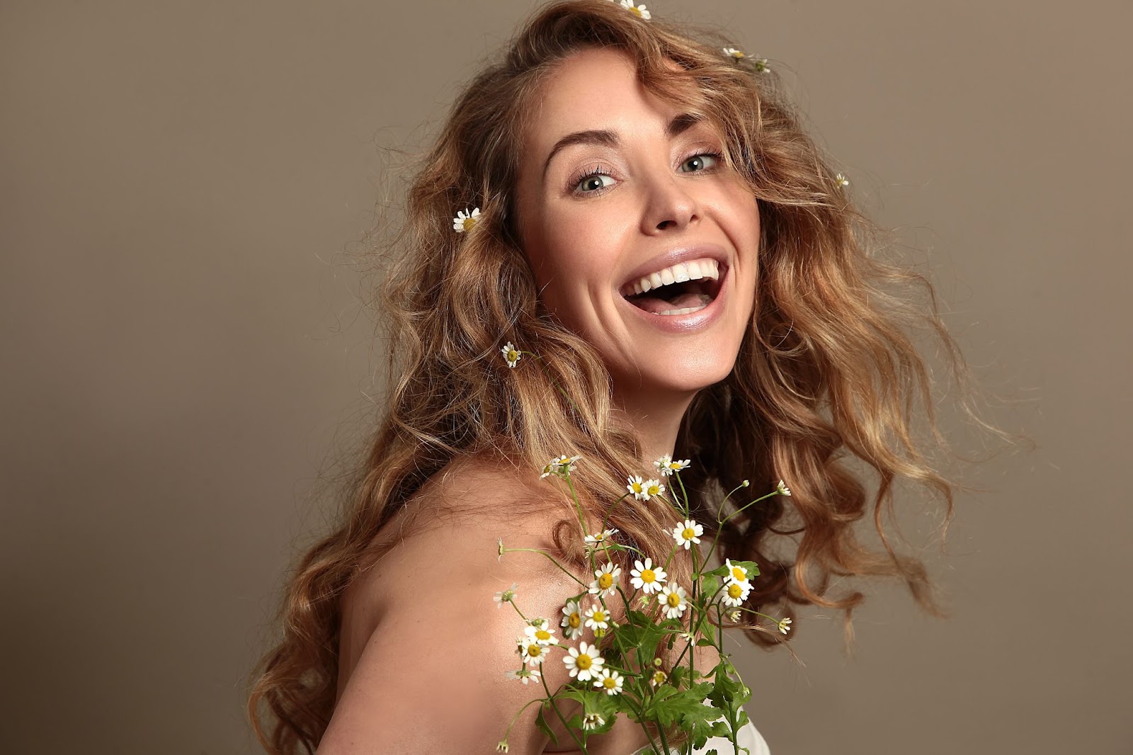 Gorgeous blonde woman smiling holding daisies with flowing skin due to her natural face skin care