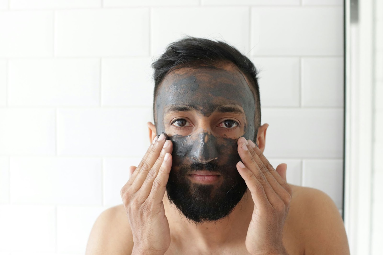 Attractive young Indian man applying a charcoal black face mask