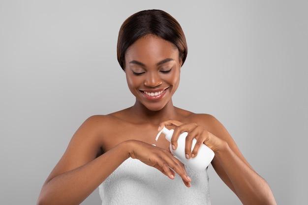 Body nourishing attractive black female applying moisturising lotion on hand