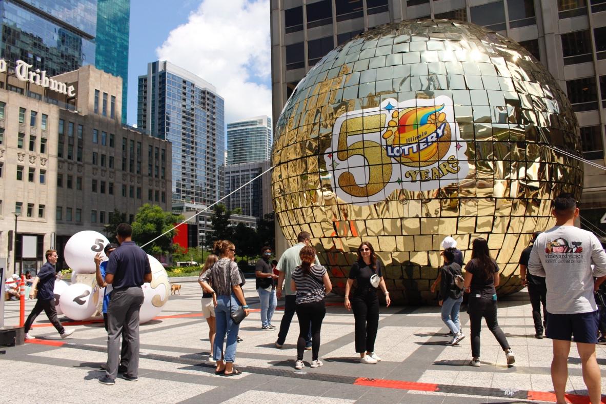 A group of people walking around a large gold ballDescription automatically generated