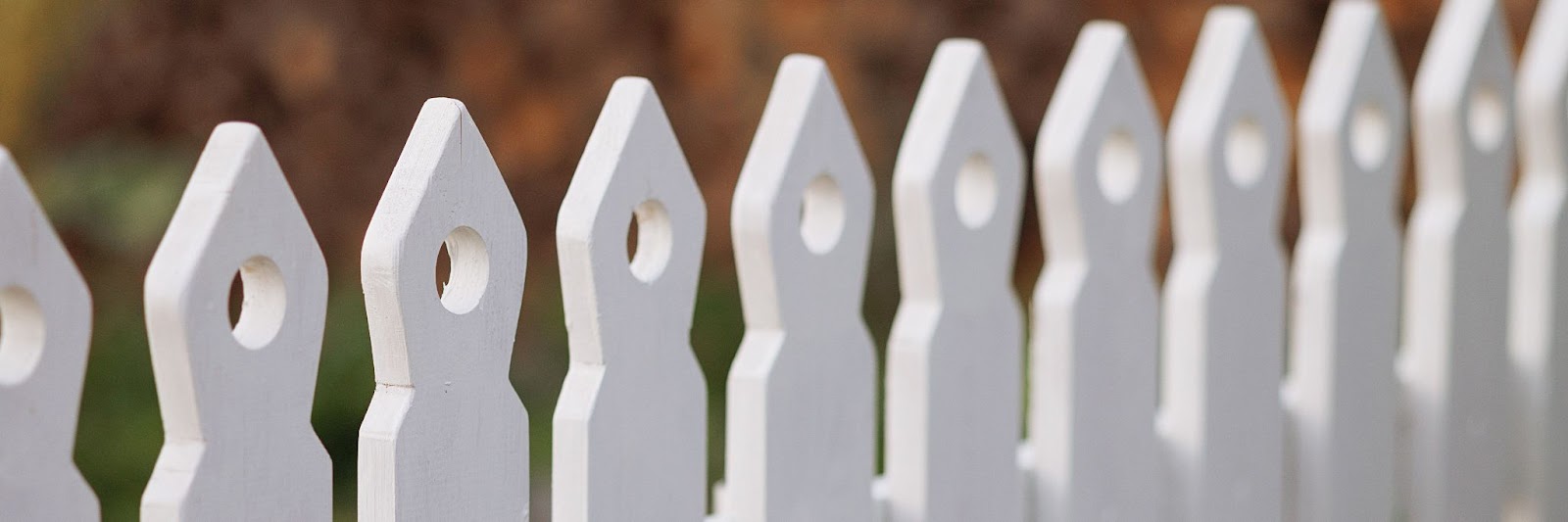 This is a close-up view of a white picket fence in a garden setting, showcasing its intricate design and texture.