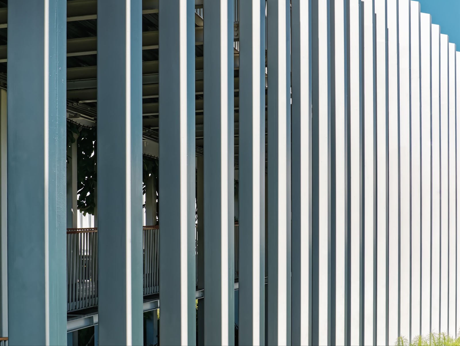 A row of vertical galvanized steel fence posts shimmering under the bright sunlight, reflecting a glossy metallic finish.